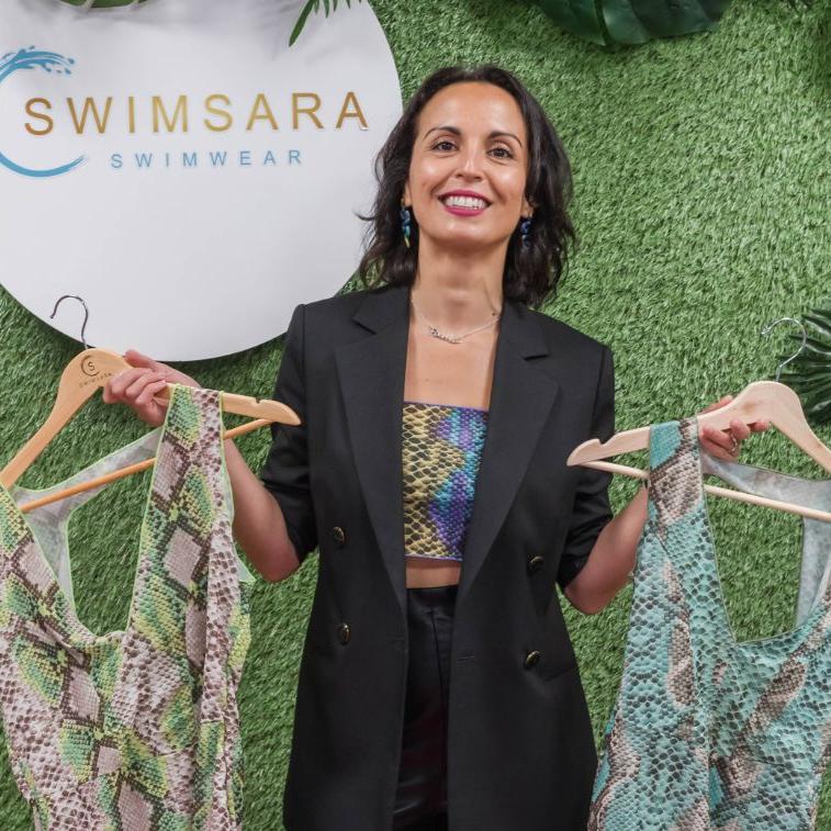 Women holding swimwear she has designed in front of back drop